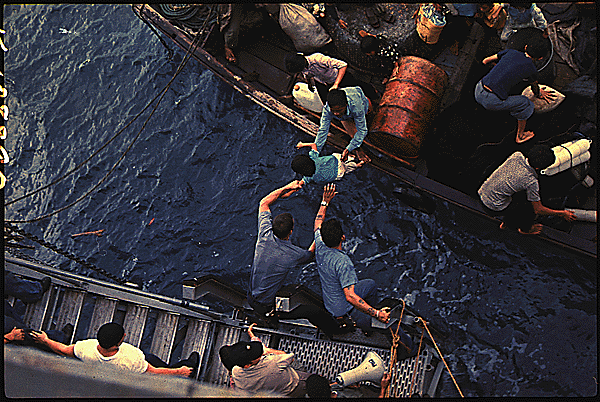 In the South China Sea, crewmen of the amphibious cargo ship USS Durham (LKA-114) take Vietnamese refugees aboard a small craft. The refugees will be transferred later by mechanized landing craft (LCM) to the freighter Transcolorado., 4/3/1975. General Records of the Department of the Navy, National Archives Identifier 558518